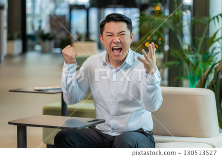 Angry mature boss arguing over video call looking at camera sitting at modern workplace in office Angry mature boss arguing over video call looking at camera sitting at modern workplace in office 130513527