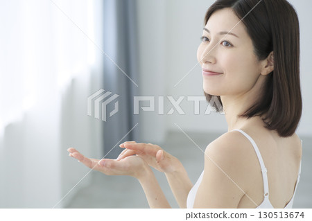 A Japanese woman applying skin care cream to her palm in the living room 130513674
