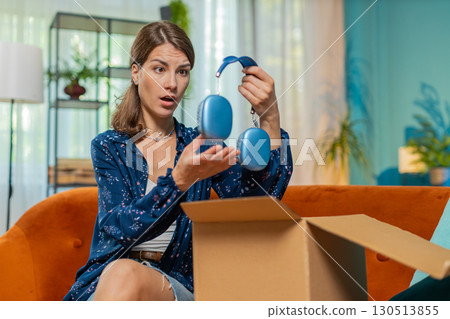 Unhappy woman unpacking carton box feels dissatisfied with damaged broken wireless headphones order 130513855