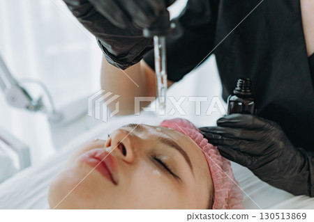 A cosmetologist is dropping serum from a dropper onto a patient's face during a cosmetic procedure 130513869