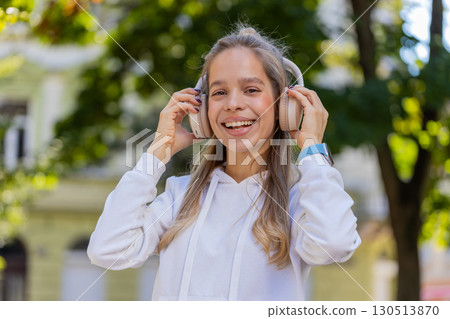 Happy young woman taking off headphones after listening favorite energetic music on city street Happy young woman taking off headphones after listening favorite energetic music on city street 130513870