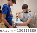 man assembling a new furniture with a screwdriver. teen age boy assisting him 130513889