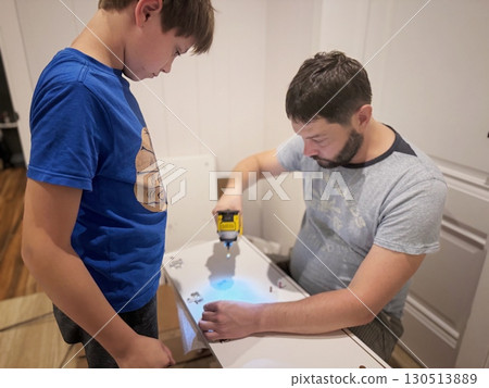 man assembling a new furniture with a screwdriver. teen age boy assisting him 130513889