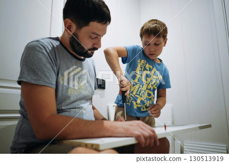 eight-year-old boy is helping his father assemble a new piece of furniture. he holds a screwdriver 130513919