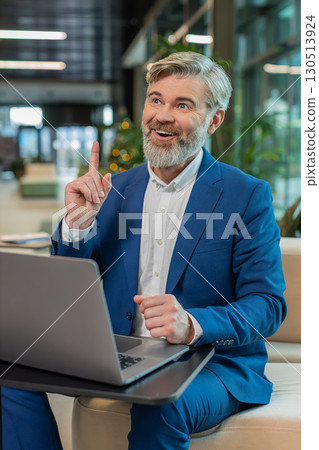 Happy businessman using laptop make gesture raises finger came up with creative plan in office lobby Happy businessman using laptop make gesture raises finger came up with creative plan in office lobby 130513924