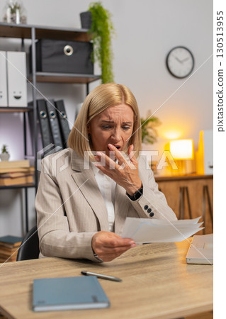 Caucasian mature businesswoman reading letters bad news feels upset sitting at home office desk 130513955