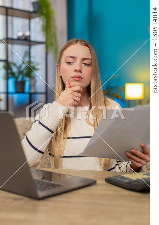 Caucasian woman managing tax declaration at home on sofa table, holding documents, calculator laptop Caucasian woman managing tax declaration at home on sofa table, holding documents, calculator laptop 130514014