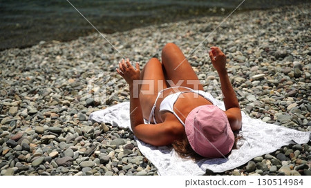 Beach sunbathing woman, woman resting on pebbles shore during summertime enjoying the sun. 130514984
