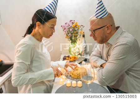 Birthday Cake Couple Celebration: Indoor intimate birthday celebration; man and woman with party hats making a wish on a cake. 130515003