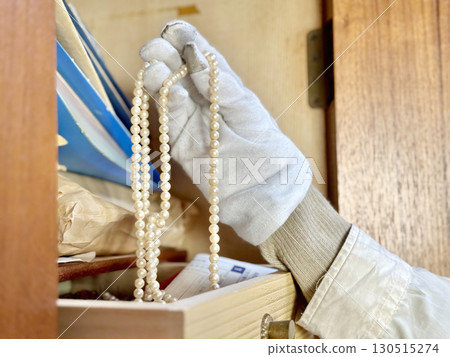 A white-gloved hand takes out a necklace from a small drawer in a dresser A white-gloved hand takes out a necklace from a small drawer in a dresser 130515274