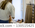 Inside a contemporary hair salon, a stylist meticulously organizes long hair extensions while a relaxed client awaits their transformation, illuminated by soft natural light. 130515425