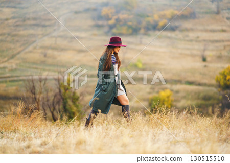 Beautiful stylish girl walks in the autumn park. The girl is dressed in a green coat and a red hat. Beautiful stylish girl walks in the autumn park. The girl is dressed in a green coat and a red hat. 130515510