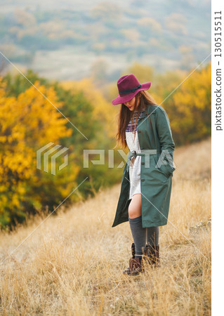 Beautiful stylish girl walks in the autumn park. The girl is dressed in a green coat and a red hat. 130515511