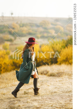 Beautiful stylish girl walks in the autumn park. The girl is dressed in a green coat and a red hat. 130515513
