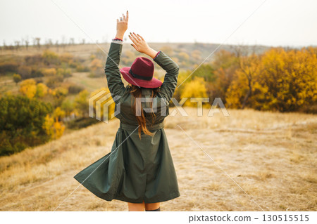 Beautiful stylish girl walks in the autumn park. The girl is dressed in a green coat and a red hat. 130515515