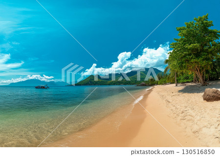 Vibrant tropical beach with golden sand, clear blue ocean, and green mountains. A small boat floats peacefully under a sunny sky with clouds. 130516850