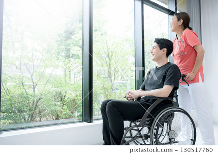A medical worker and a wheelchair patient surrounded by beautiful greenery by the window A medical worker and a wheelchair patient surrounded by beautiful greenery by the window 130517760