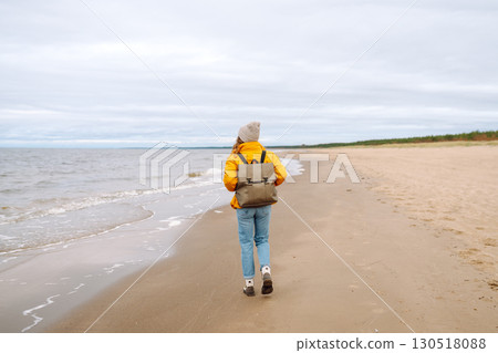 Attractive woman on windy cold beach. Beautiful tourist woman in stylish clothes enjoys life by sea. Attractive woman on windy cold beach. Beautiful tourist woman in stylish clothes enjoys life by sea. 130518088