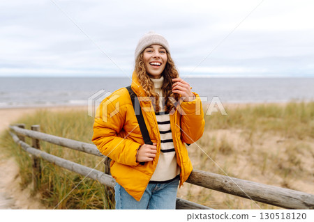 A beautiful young tourist woman in a yellow jacket with a backpack enjoys life near the sea. Travel. A beautiful young tourist woman in a yellow jacket with a backpack enjoys life near the sea. Travel. 130518120