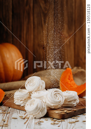 Pumpkin marshmallow sweets with powdered sugar falling, rustic autumn wooden background 130518128