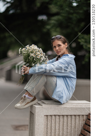 Daisies Bouquet Woman: Girl sits holding flowers on sunny day outdoors during spring, feeling relaxed. Daisies Bouquet Woman: Girl sits holding flowers on sunny day outdoors during spring, feeling relaxed. 130518230