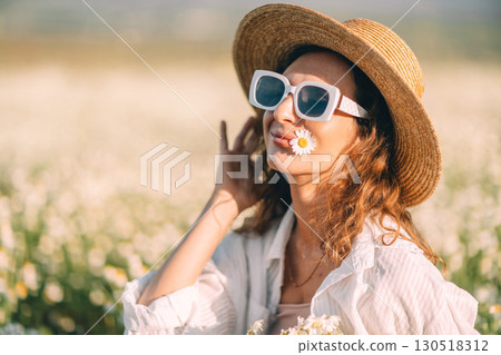 Daisy Field Hat: Woman relaxes in a sunny chamomile field, enjoying springtime. 130518312