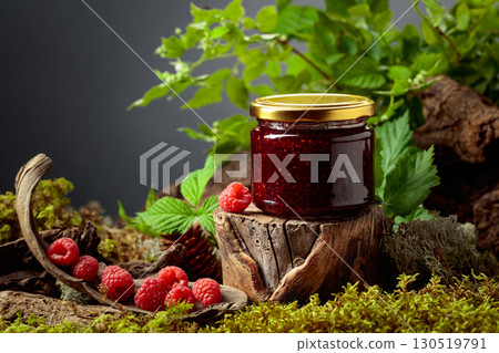 A jar of raspberry jam with fresh berries on an old tree trunk in the forest. 130519791