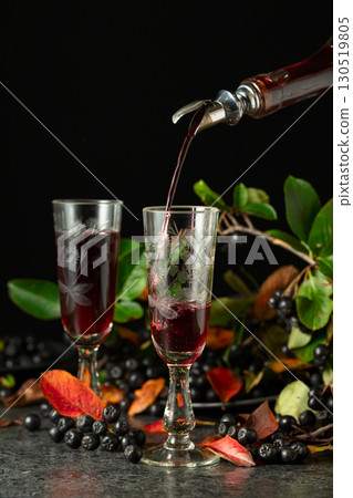 Black chokeberry drink is poured from a bottle into a glass. 130519805