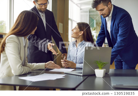 Team of business people meeting by office table, working with documents, talking and using laptop Team of business people meeting by office table, working with documents, talking and using laptop 130519835