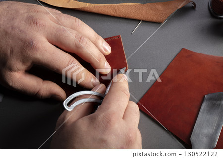 The process of making leather goods. The hands of the master work with a leather product. The process of making leather goods. The hands of the master work with a leather product. 130522122