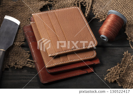 Making leather wallets. On a wooden table there are leather wallets, a spool of thread and a knife. Making leather wallets. On a wooden table there are leather wallets, a spool of thread and a knife. 130522417