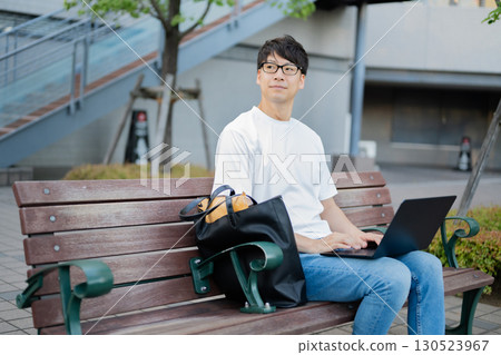 Man using a laptop on a bench Man using a laptop on a bench 130523967