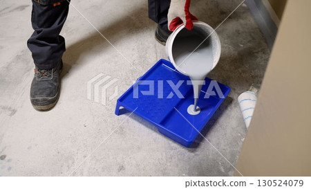 Painter pouring white paint into a tray 130524079
