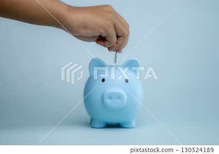 A hand is dropping coins into a piggy bank. The concept of saving and investing. A hand is dropping coins into a piggy bank. The concept of saving and investing. 130524189