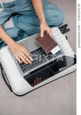 Person using a laptop on a suitcase with a passport, symbolizing travel planning or remote work. Person using a laptop on a suitcase with a passport, symbolizing travel planning or remote work. 130524238