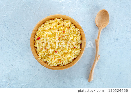 Cooked millet in a wooden bowl on a blue background, with a spoon 130524466