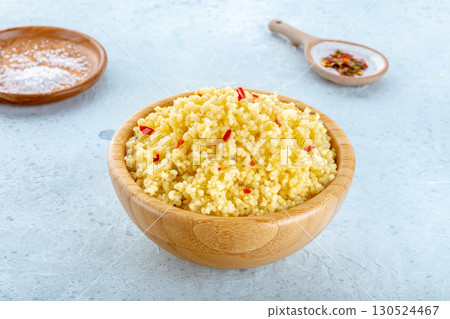 Cooked millet in a wooden bowl on a blue background, with salt and pepper 130524467