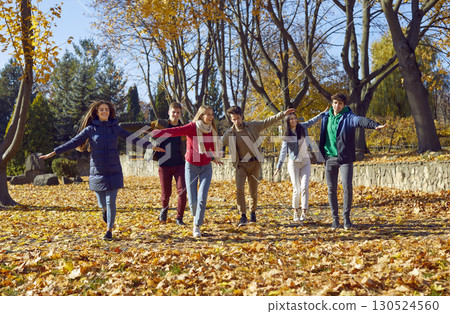 Happy smiling friends enjoy walking through the autumn park, running with their arms outstretched to sides on sunny warm day. Happy smiling friends enjoy walking through the autumn park, running with their arms outstretched to sides on sunny warm day. 130524560
