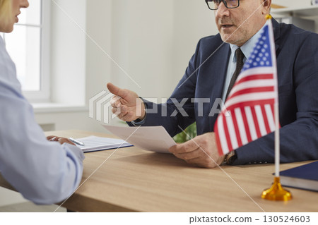 USA consul sitting at desk with American flag and talking to woman about visa application 130524603