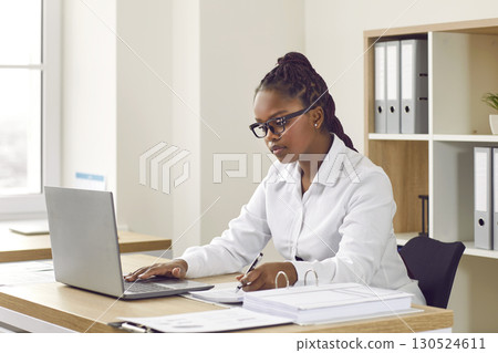 Focused African woman working on laptop at her desk in modern office 130524611