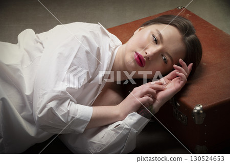 A beautiful girl lies on an old suitcase on a gray background. A beautiful girl lies on an old suitcase on a gray background. 130524653