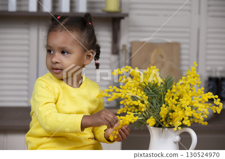 Little African American girl with yellow flowers on a gray background. 130524970