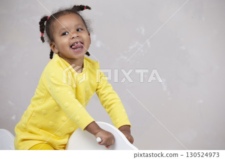 Little African American girl in yellow clothes shows tongue. Funny child. Little African American girl in yellow clothes shows tongue. Funny child. 130524973