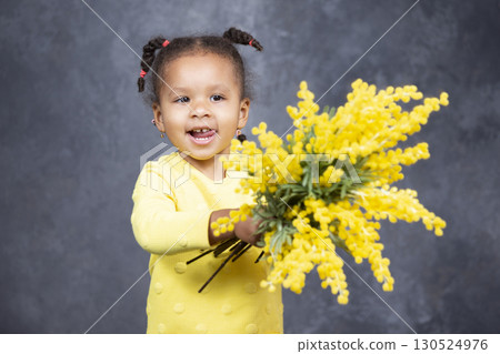 Little African American girl with yellow flowers on a gray background. 130524976