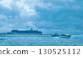 A small boat sailing through the cloudy sea with a large cruise ship in the distance 130525112