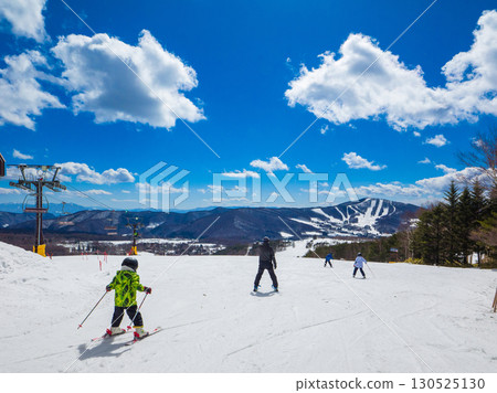 A family skiing down a slope on a clear winter day, with snowy scenery (Nagano Prefecture, Ueda City, Sugadaira Plateau) 130525130