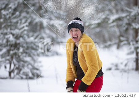 Happy middle-aged woman throws snow and laughs cheerfully. An adult woman on a walk in the winter forest. Happy middle-aged woman throws snow and laughs cheerfully. An adult woman on a walk in the winter forest. 130525437