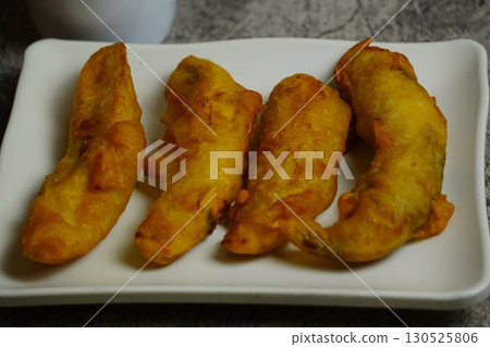 Close-up of freshly Pisang Goreng or fried Indonesian banana fritters on a white plate. A popular sweet snack or dessert. 130525806