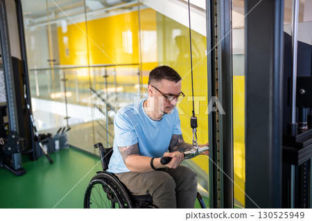 Man in wheelchair do vertical pull workout using adaptive sport machine for para athletes in gym 130525949