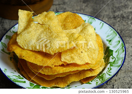 Golden and crispy opak or Indonesian Cassava Crackers on a vintage enamel plate. A popular savory snack with a crunchy texture. Golden and crispy opak or Indonesian Cassava Crackers on a vintage enamel plate. A popular savory snack with a crunchy texture. 130525965